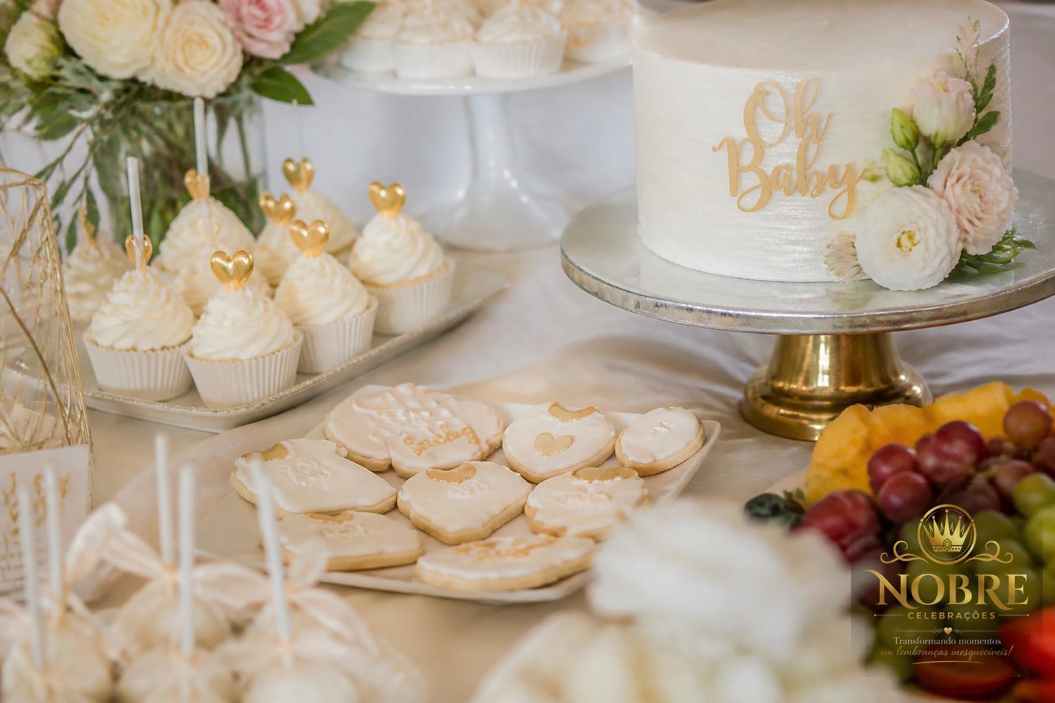Mesa de doces de chá de bebê em detalhe com cupcakes, biscoitos decorados, bolo, frutas, bandejas e flores naturais