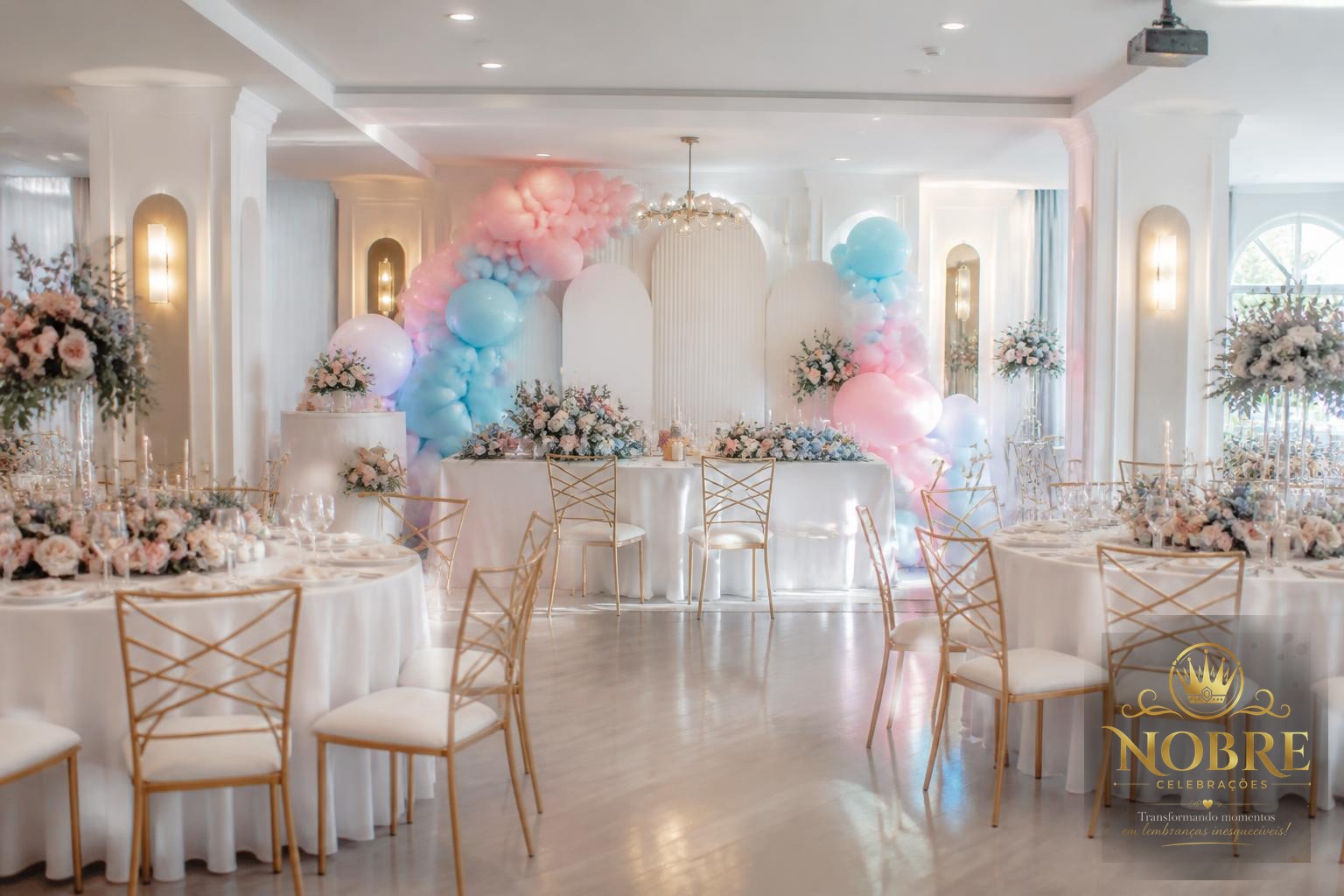 Salão elegante preparado para chá revelação com mesas dos convidados, cadeiras sofisticadas, balões, flores naturais e painel decorativo